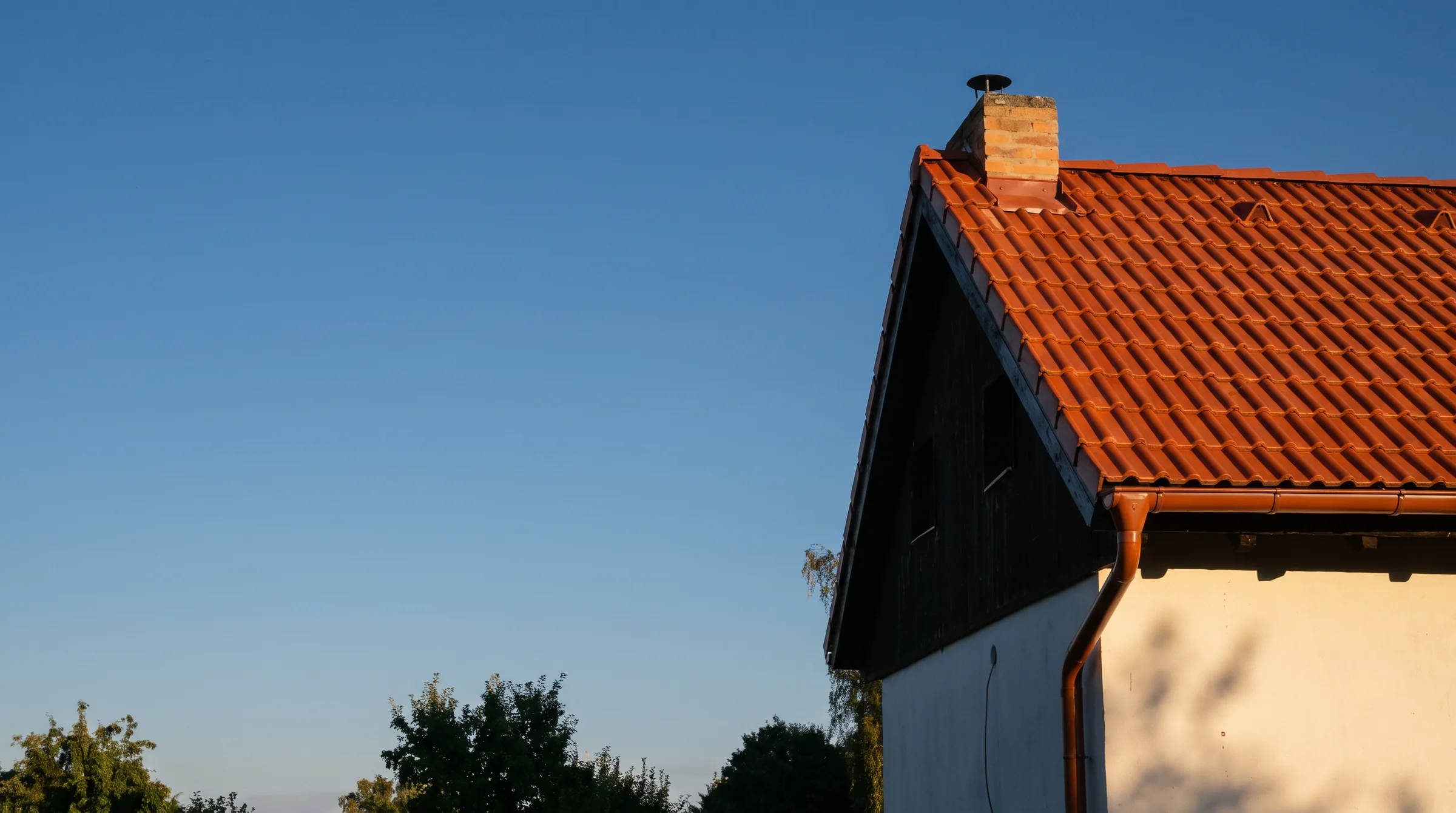 Nová střecha z pálených tašek s měděným okapem ve večerním slunci